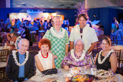 A group of six, four seated and two standing, pose for a photograph near an event table.