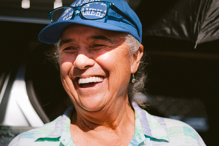 A person wearing a blue hat smiles brightly in the sunshine.