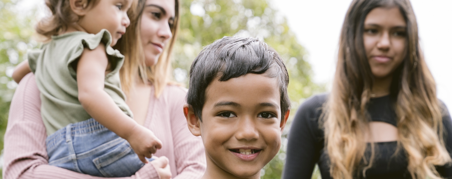 Young boy smiling with two young girls in the background and a toddler