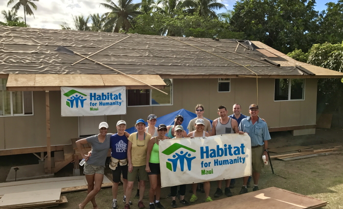A smiing group of Habitat for Humanity Maui volunteers posing in front of a house they helped build