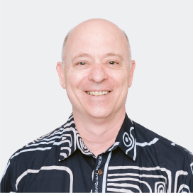 A man smiles, wearing a black collared shirt with white swirling designs.