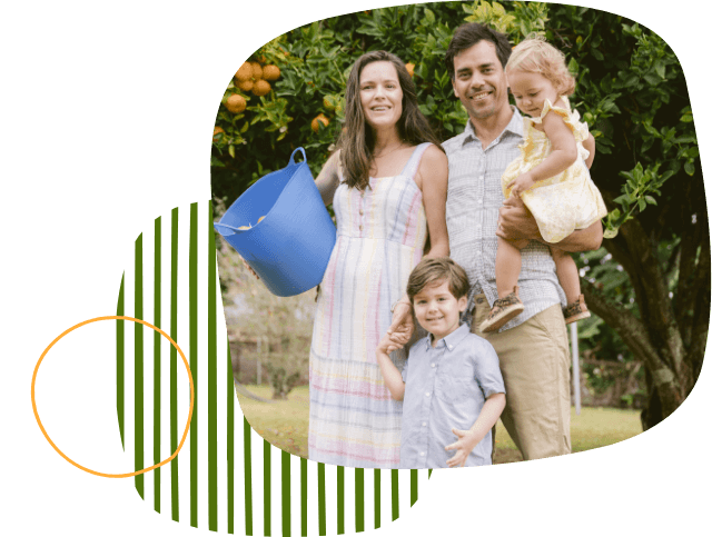A family smiling together while standing in front of an orange orchard