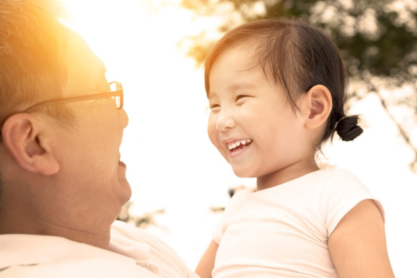 A young child smiles at a man wearing glasses who is also smiling at her while holding her.